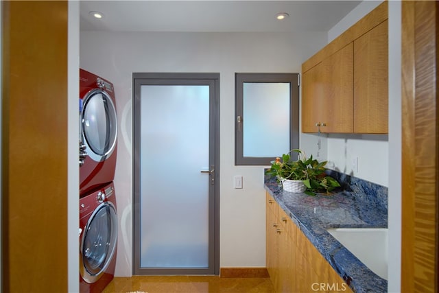 washroom with cabinets, stacked washing maching and dryer, and sink