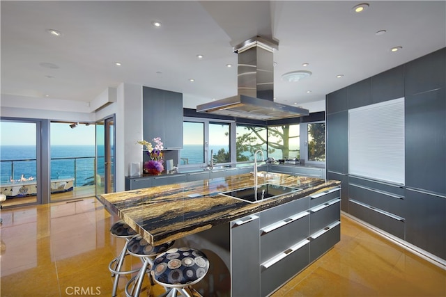 kitchen featuring a water view, a kitchen island with sink, island exhaust hood, sink, and light tile patterned floors