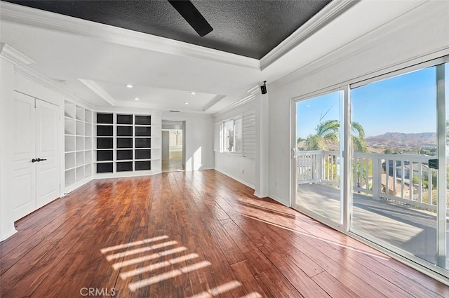 unfurnished living room with a mountain view, a raised ceiling, crown molding, and a wealth of natural light