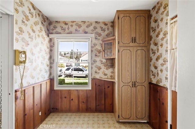 interior space featuring wallpapered walls, wood walls, light floors, and wainscoting