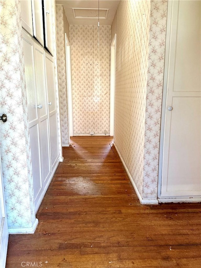 hall with wallpapered walls, attic access, baseboards, and dark wood-style flooring