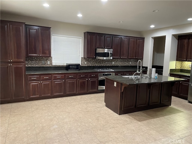 kitchen with sink, appliances with stainless steel finishes, a kitchen island with sink, and tasteful backsplash