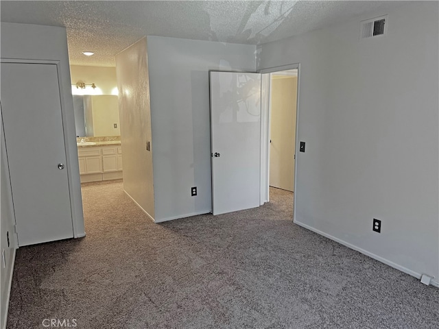 unfurnished bedroom featuring a textured ceiling, ensuite bath, and carpet flooring