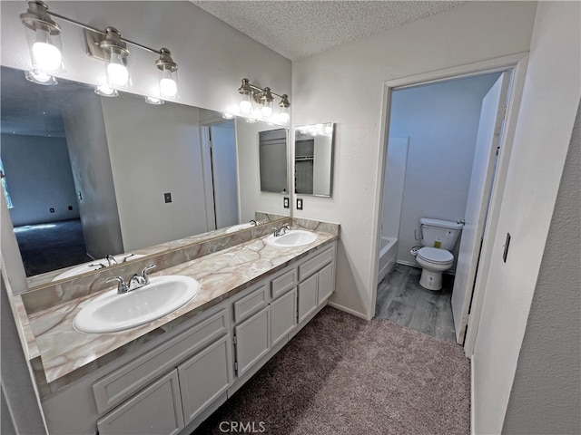 bathroom with a textured ceiling, vanity, toilet, and a tub