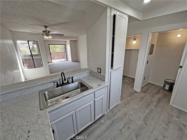 kitchen with ceiling fan, white cabinets, sink, a textured ceiling, and light hardwood / wood-style floors