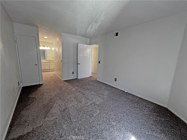 unfurnished bedroom featuring dark carpet, ensuite bath, and a textured ceiling