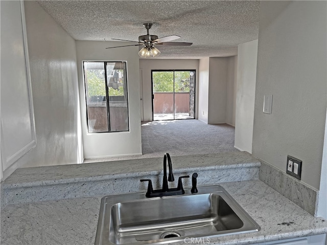 kitchen with a textured ceiling, carpet flooring, sink, light stone countertops, and ceiling fan