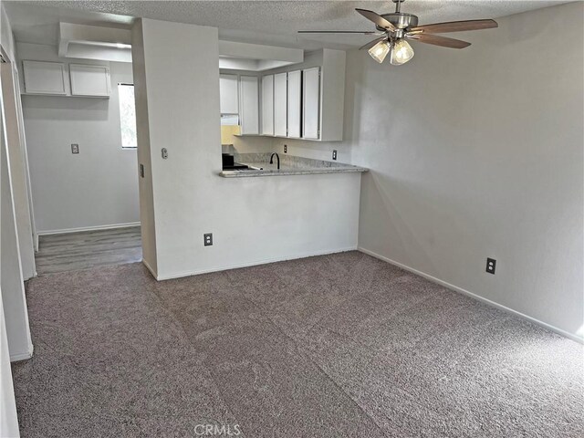 kitchen with a textured ceiling, carpet flooring, and white cabinetry