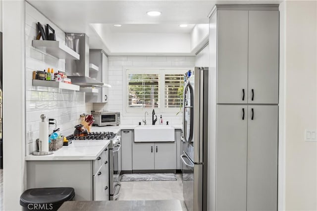 kitchen featuring wall chimney exhaust hood, sink, appliances with stainless steel finishes, a tray ceiling, and decorative backsplash