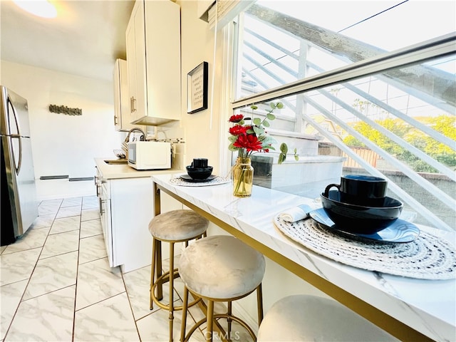 kitchen with a kitchen breakfast bar, white cabinetry, and stainless steel refrigerator