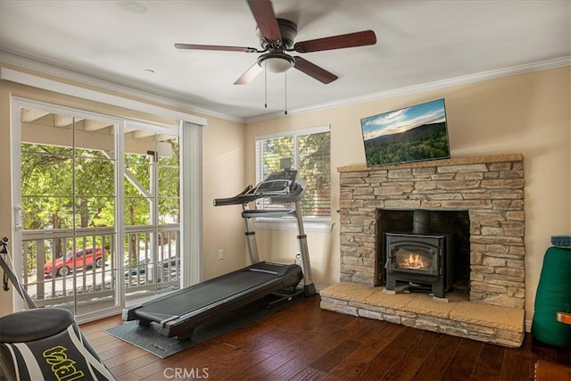 exercise room with ceiling fan, crown molding, dark wood-type flooring, and a wood stove