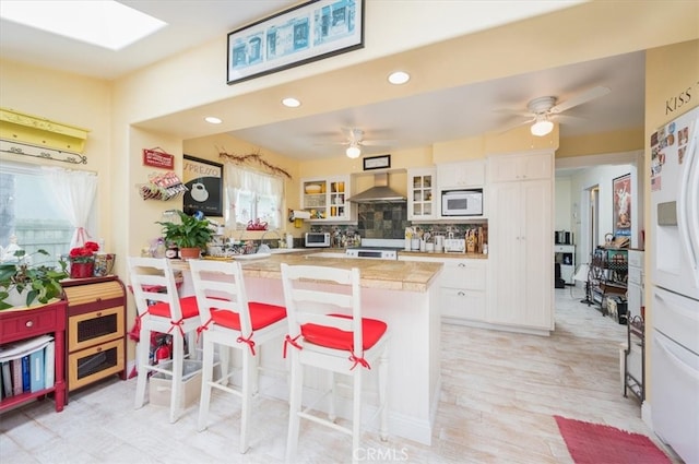 kitchen featuring white cabinets, wall chimney exhaust hood, white appliances, and a healthy amount of sunlight