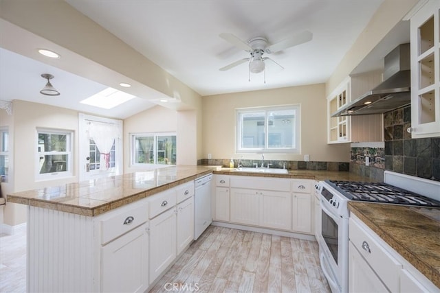 kitchen featuring wall chimney exhaust hood, white appliances, plenty of natural light, and kitchen peninsula