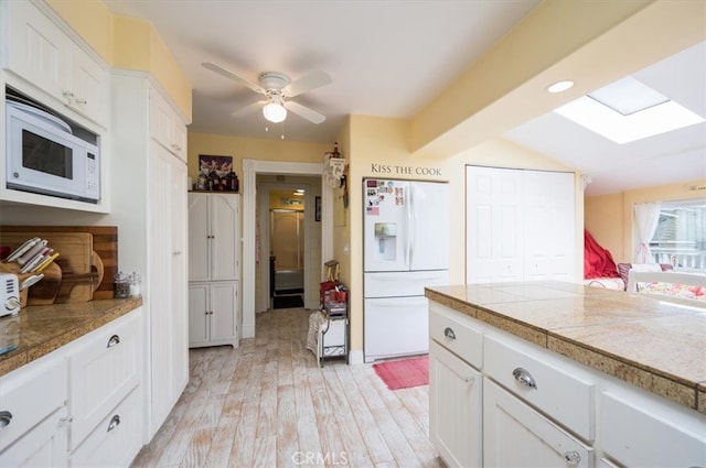 kitchen featuring light hardwood / wood-style floors, white cabinetry, white appliances, vaulted ceiling with skylight, and ceiling fan