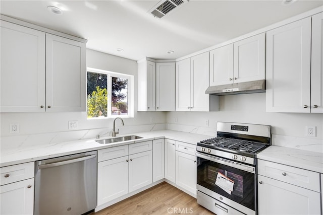 kitchen with appliances with stainless steel finishes, light hardwood / wood-style floors, white cabinetry, light stone counters, and sink