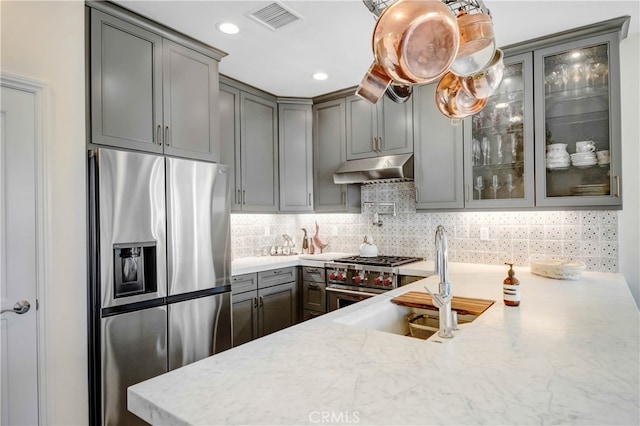 kitchen with tasteful backsplash, hanging light fixtures, light stone counters, sink, and stainless steel appliances