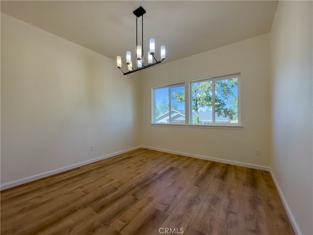 spare room with an inviting chandelier and wood-type flooring