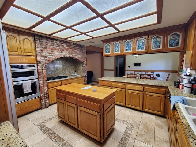 kitchen with kitchen peninsula, decorative backsplash, light tile patterned floors, a kitchen island, and stainless steel double oven