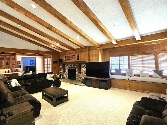 living room with wooden walls, vaulted ceiling with beams, a fireplace, a textured ceiling, and carpet floors