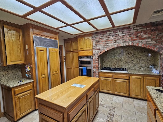 kitchen with gas stovetop, tasteful backsplash, light stone counters, double oven, and light tile patterned floors