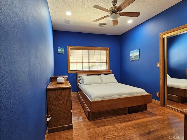 bedroom with ceiling fan, wood-type flooring, and a textured ceiling