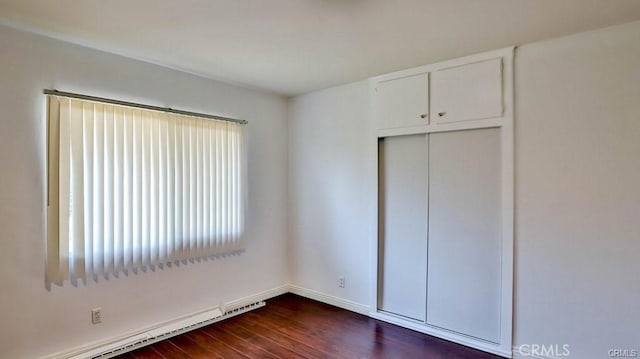 unfurnished bedroom with a baseboard radiator, a closet, and dark wood-type flooring