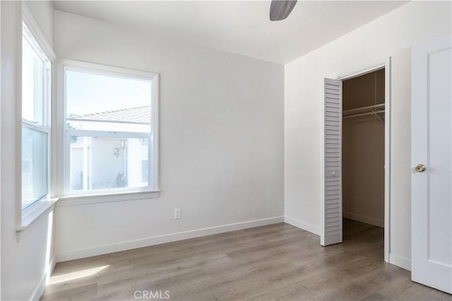 unfurnished bedroom featuring ceiling fan, a walk in closet, light hardwood / wood-style floors, and a closet