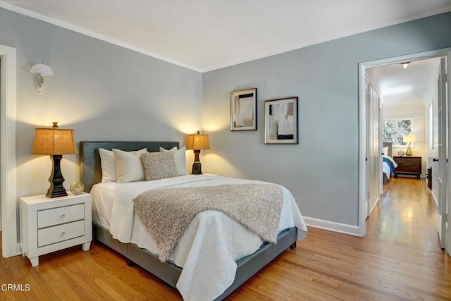 bedroom with light wood finished floors, crown molding, and baseboards