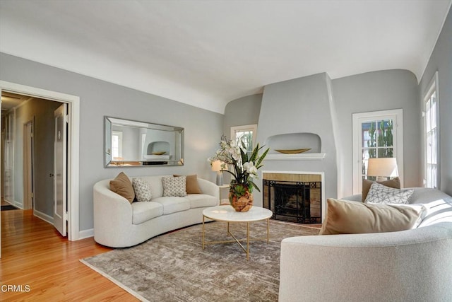 living area featuring vaulted ceiling, a fireplace, baseboards, and wood finished floors