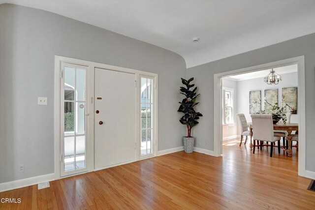 foyer entrance with light wood finished floors, visible vents, an inviting chandelier, and baseboards