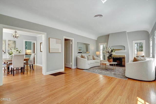 living room featuring visible vents, baseboards, a fireplace, light wood-type flooring, and a chandelier