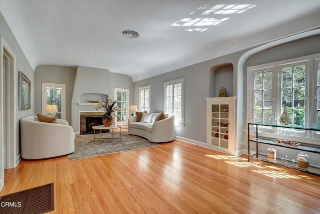 living room with visible vents, wood finished floors, baseboards, a large fireplace, and lofted ceiling