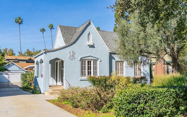 view of front of property with stucco siding, a shingled roof, a detached garage, and a gate