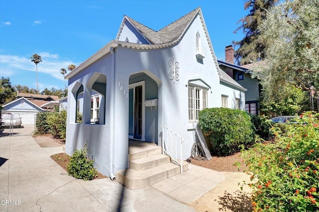 view of front facade featuring an outbuilding, a chimney, and stucco siding