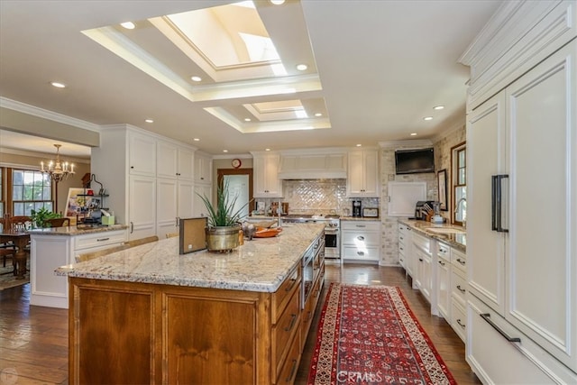 kitchen featuring a skylight, a kitchen island, white cabinetry, dark hardwood / wood-style floors, and crown molding