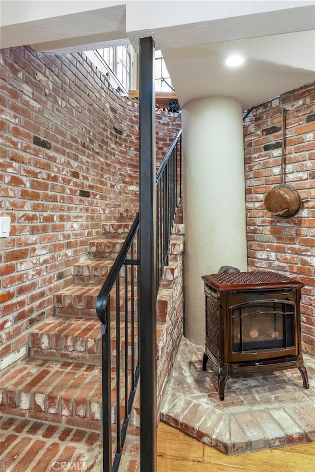 stairway featuring brick wall, hardwood / wood-style flooring, and a wood stove