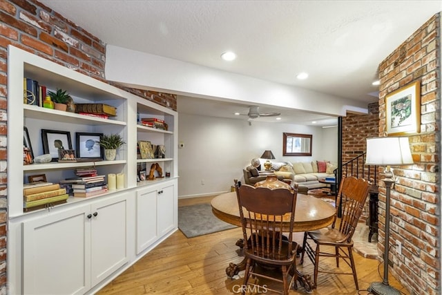 dining room with light wood-type flooring, a textured ceiling, ceiling fan, and brick wall