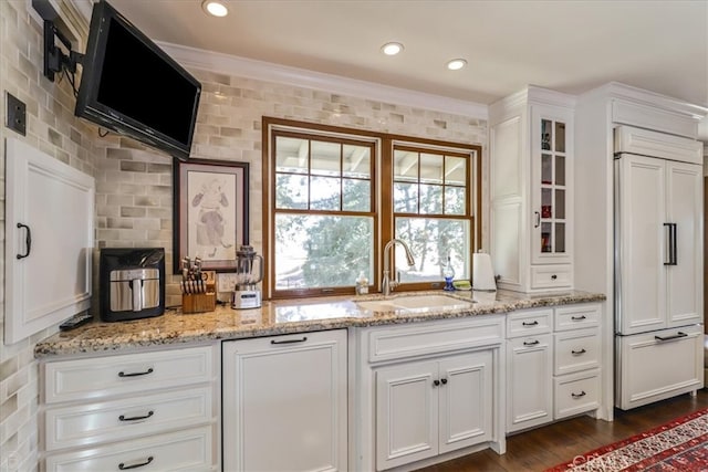 kitchen with white cabinetry, light stone counters, paneled built in refrigerator, ornamental molding, and sink