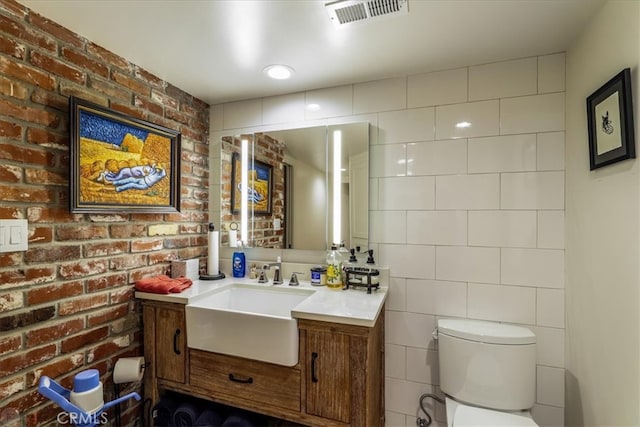 bathroom with brick wall, vanity, and toilet