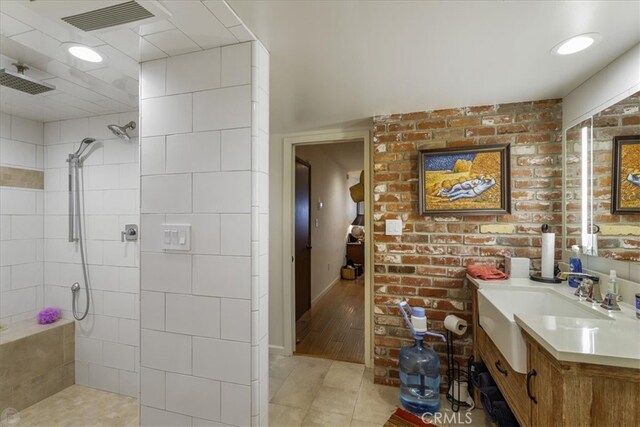 bathroom with a tile shower, vanity, wood-type flooring, and brick wall