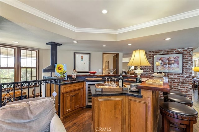 kitchen with wine cooler, an island with sink, ornamental molding, kitchen peninsula, and dark hardwood / wood-style floors