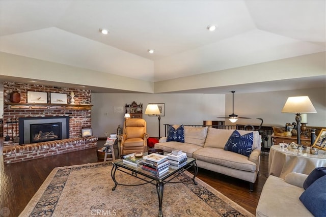 living room with vaulted ceiling, ceiling fan, dark wood-type flooring, and a brick fireplace