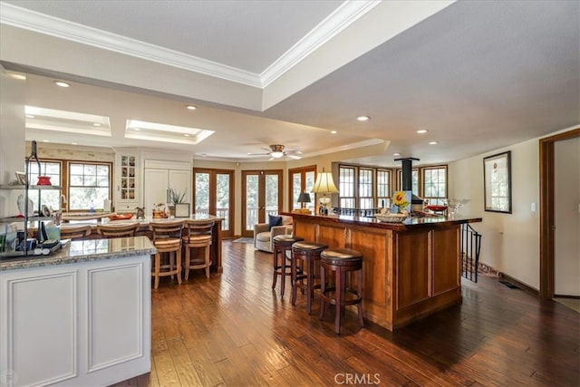 bar with light stone counters, dark wood-type flooring, ornamental molding, ceiling fan, and french doors