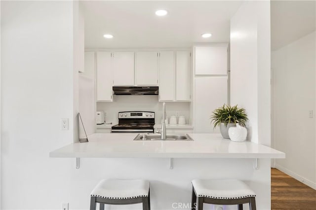 kitchen with under cabinet range hood, dark wood-style flooring, white cabinetry, a kitchen bar, and stainless steel range with electric stovetop