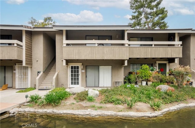 rear view of property featuring a water view, stairs, and stucco siding