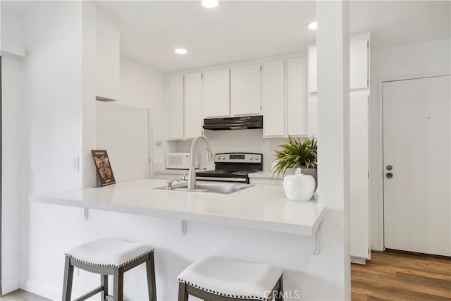 kitchen featuring a peninsula, white appliances, a breakfast bar area, and under cabinet range hood