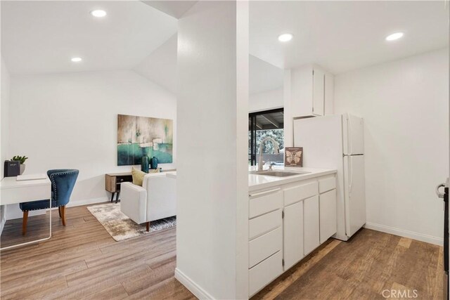 kitchen with light hardwood / wood-style floors, white cabinetry, white refrigerator, lofted ceiling, and sink