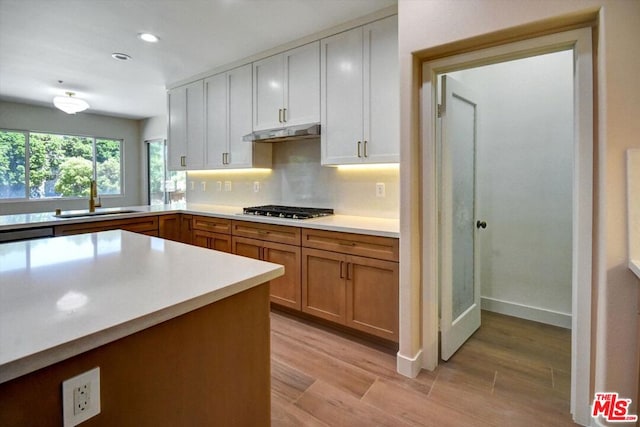 kitchen featuring white cabinets, sink, backsplash, stainless steel gas stovetop, and light hardwood / wood-style floors