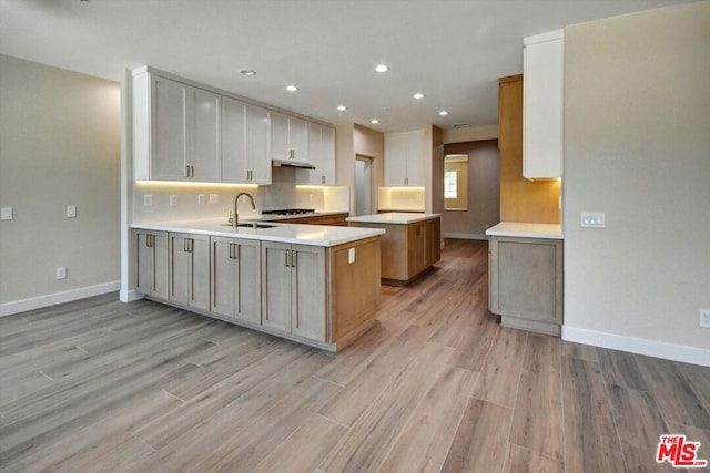 kitchen with a center island, white cabinets, sink, kitchen peninsula, and light hardwood / wood-style flooring