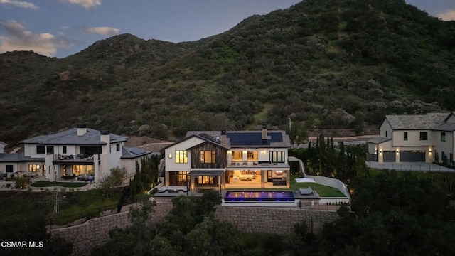 back house at dusk featuring a mountain view, a balcony, and solar panels